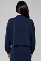 Back view of a woman wearing a dark navy blue long-sleeve top and matching drawstring skirt against a neutral beige background.