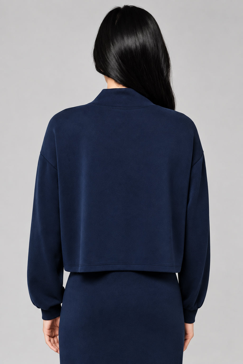Back view of a woman wearing a dark navy blue long-sleeve top and matching drawstring skirt against a neutral beige background.