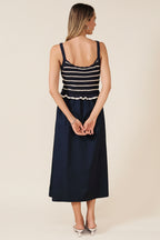 Back view of a woman wearing a navy and white crochet striped top with a navy skirt on a beige background