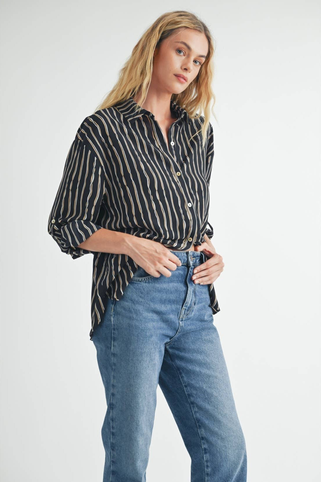 Woman wearing a black blouse with ivory and tan stripes and blue jeans on a white background
