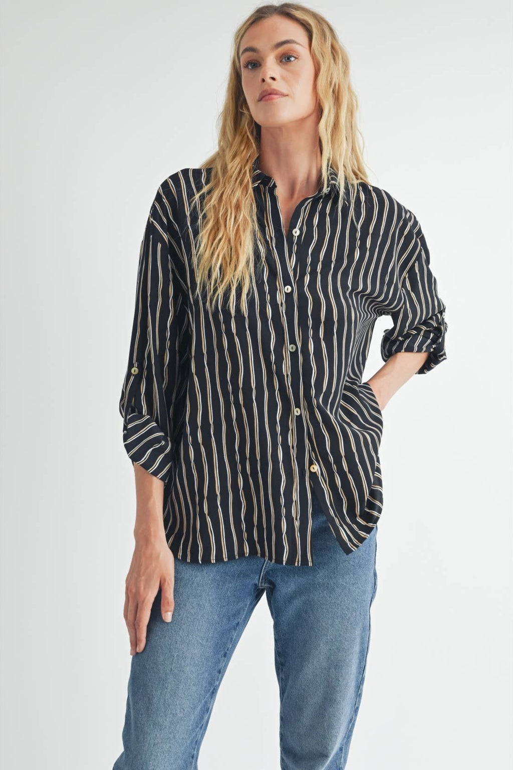 Woman wearing a black blouse with ivory and tan stripes and blue jeans on a white background