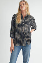 Woman wearing a black blouse with ivory and tan stripes and blue jeans on a white background