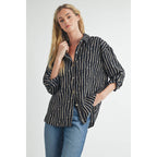 Woman wearing a black blouse with ivory and tan stripes and rolled-up sleeves with button tab on a white background