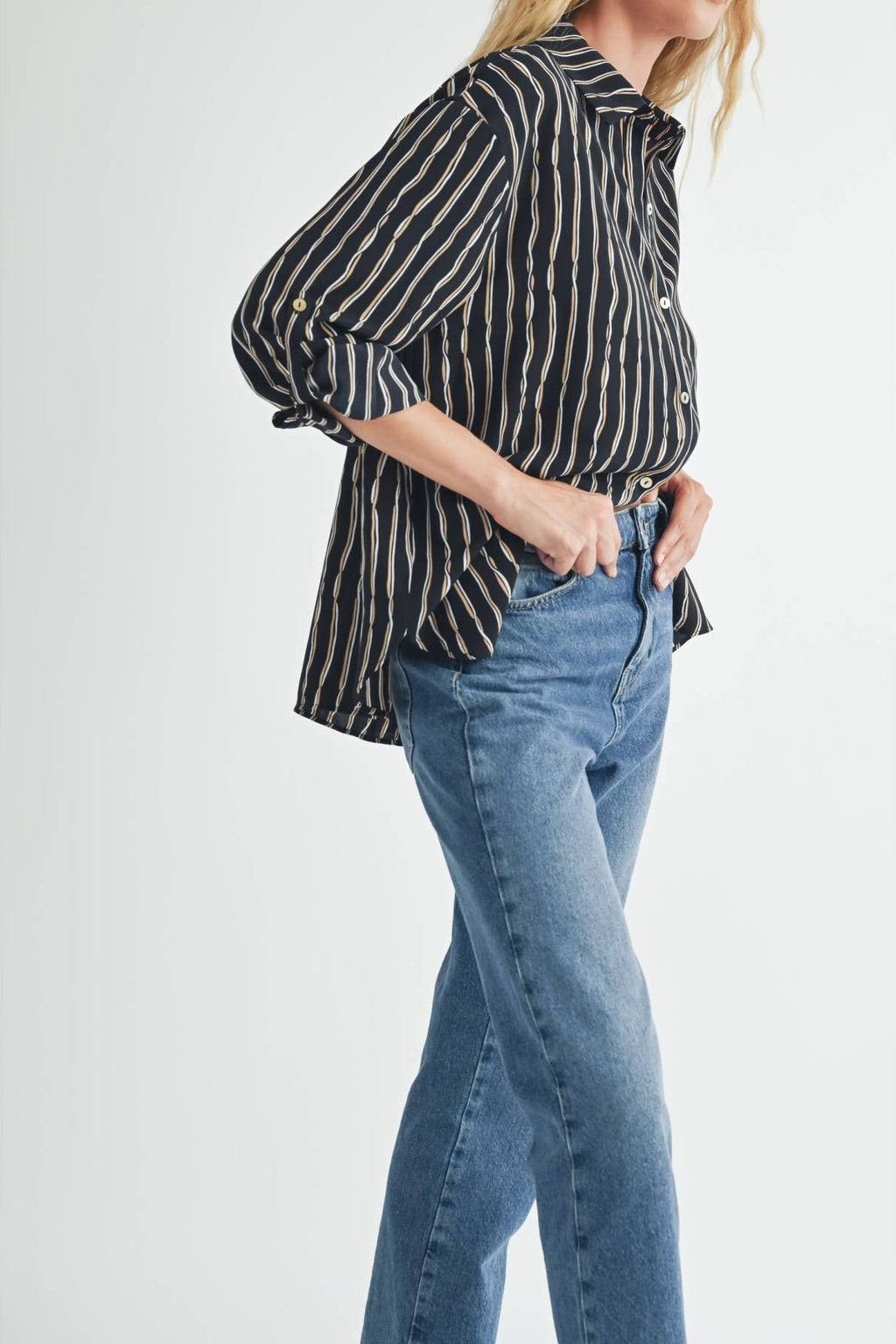 Woman wearing a striped blouse of ivory and tan on black background and blue jeans on a light gray background