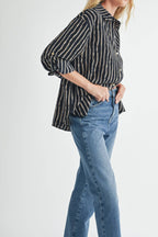 Woman wearing a striped blouse of ivory and tan on black background and blue jeans on a light gray background