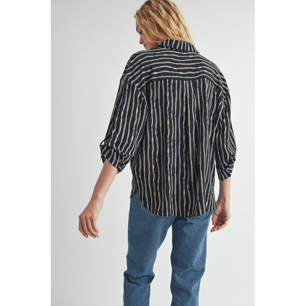 Woman wearing a black blouse with ivory and tan stripes and blue jeans on a plain background