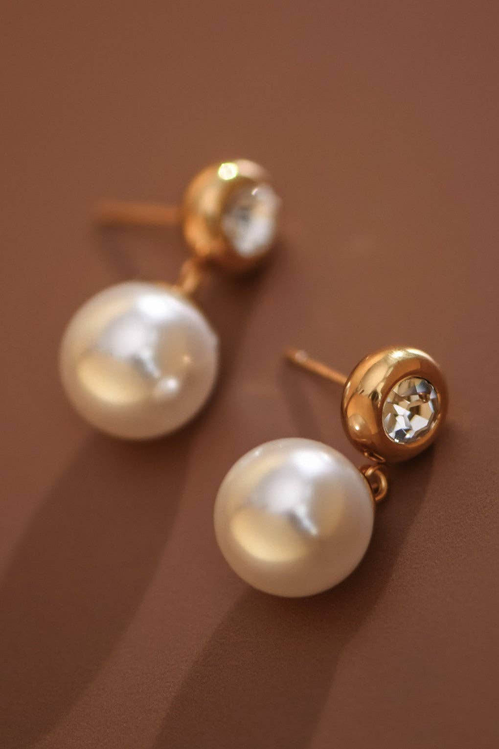 Pearl drop earrings with CZ gold stud post on a brown background