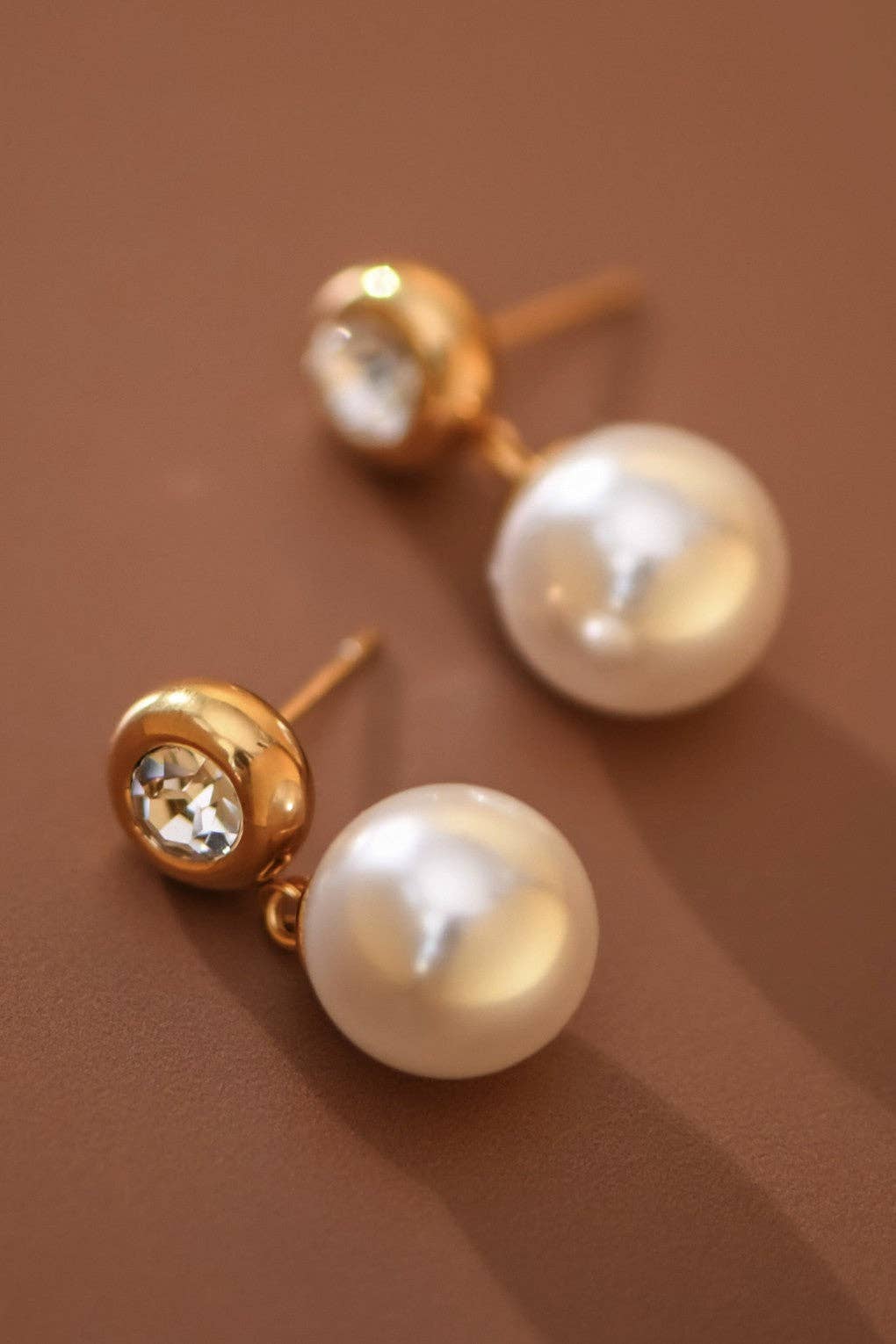 Pearl drop earrings with CZ gold stud post on a brown background