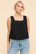 Woman wearing a black square neckline tank top and blue jeans on a beige background
