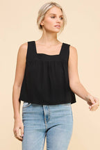 Woman wearing a black square neckline tank top and blue jeans on a beige background