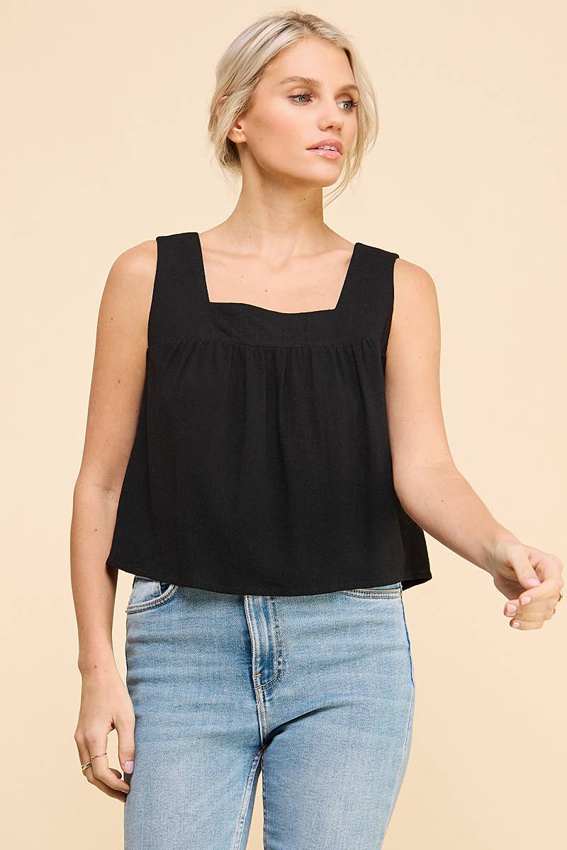 Woman wearing a black square neckline tank top and blue jeans on a beige background