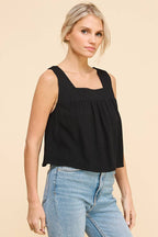 Woman wearing a black square neckline tank top and blue jeans on a beige background