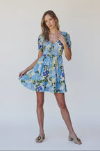 Woman wearing a floral dress with blue, green, and white colors in an outdoor setting