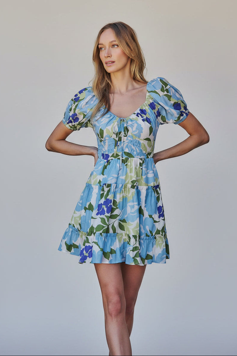Woman wearing a floral dress with blue, green, and white colors in an outdoor setting