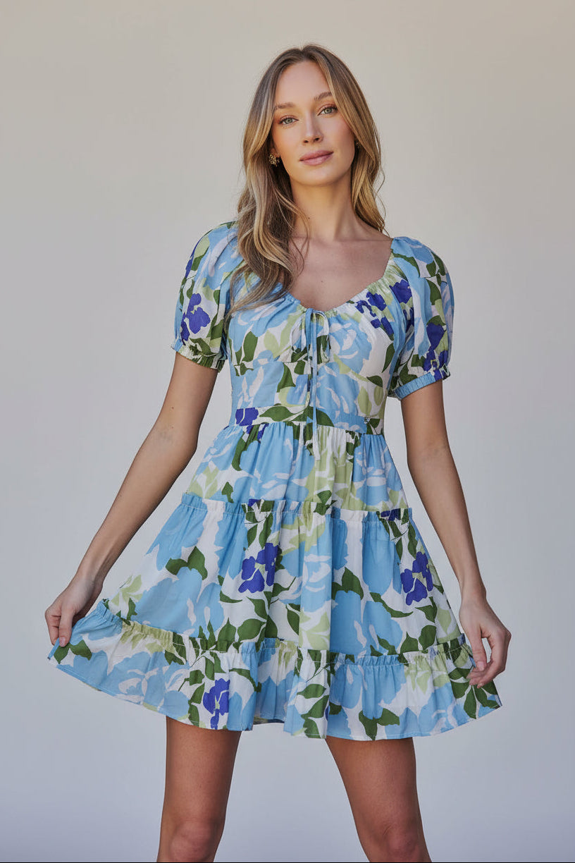 Woman wearing a floral dress with blue, green, and white colors in an outdoor setting