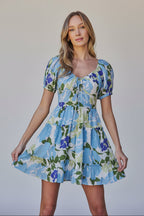Woman wearing a floral dress with blue, green, and white colors in an outdoor setting