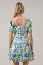 Back view of a woman wearing a floral dress with blue, green, and white colors on a grey background