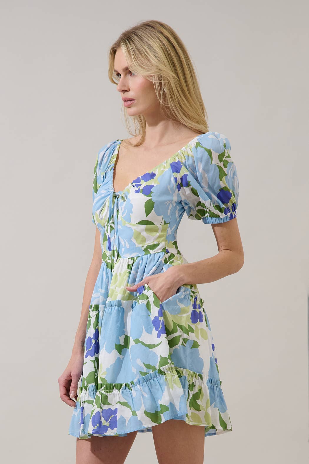 Woman wearing a floral dress with blue, green, and white colors on a grey background