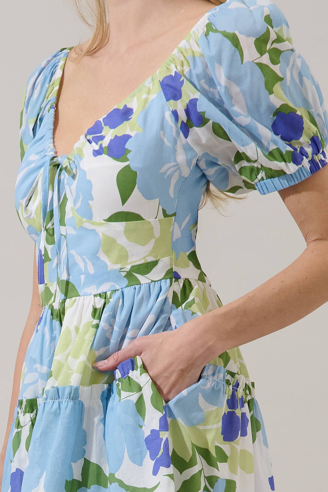 Woman wearing a floral dress with blue, green, and white colors on a plain background