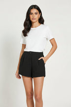 Woman wearing black classic shorts with front  pleats and white top on white background