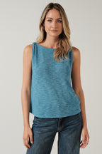 Woman wearing a blue turquoise sleeveless top and jeans against a beige background