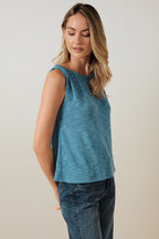 Woman wearing a blue turquoise sleeveless top and jeans against a beige background