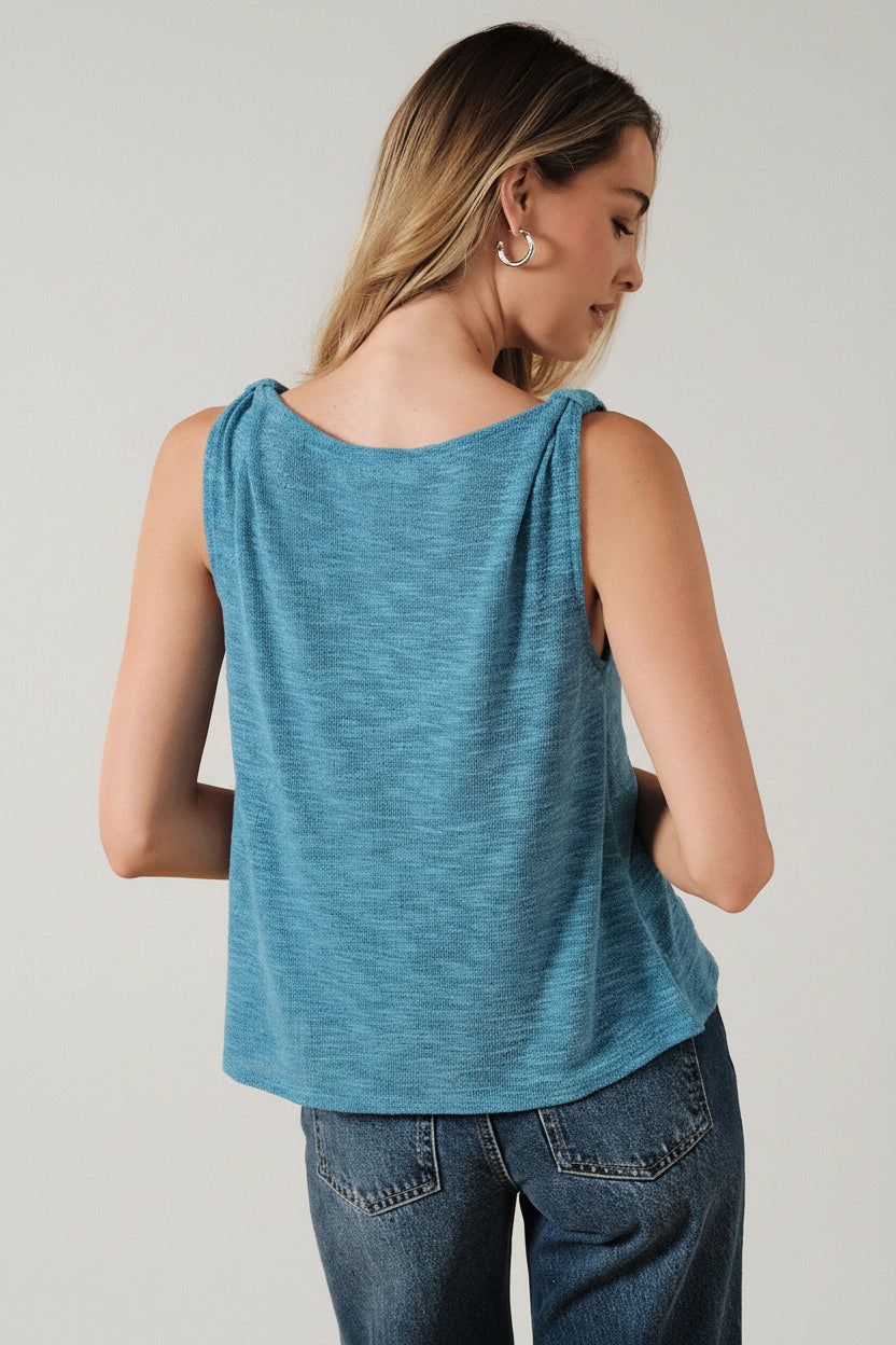 Back view of a woman wearing a blue turquoise sleeveless top and jeans on a beige background