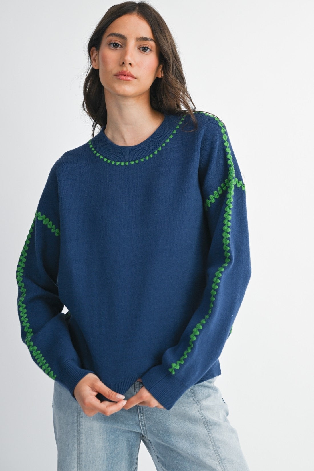 Woman wearing a royal blue sweater with green stitching on a white background