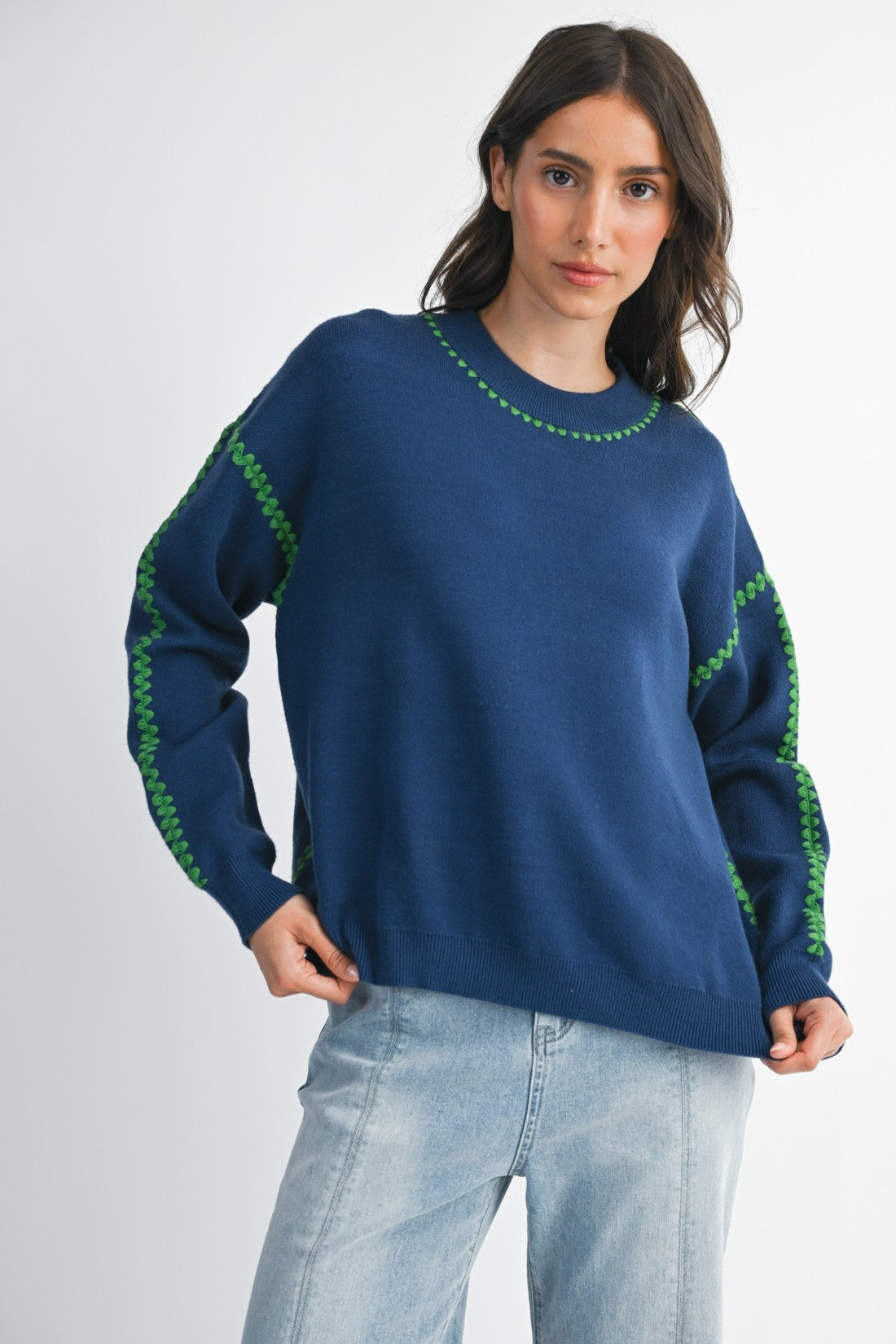 Woman wearing a royal blue sweater with green stitching on a white background