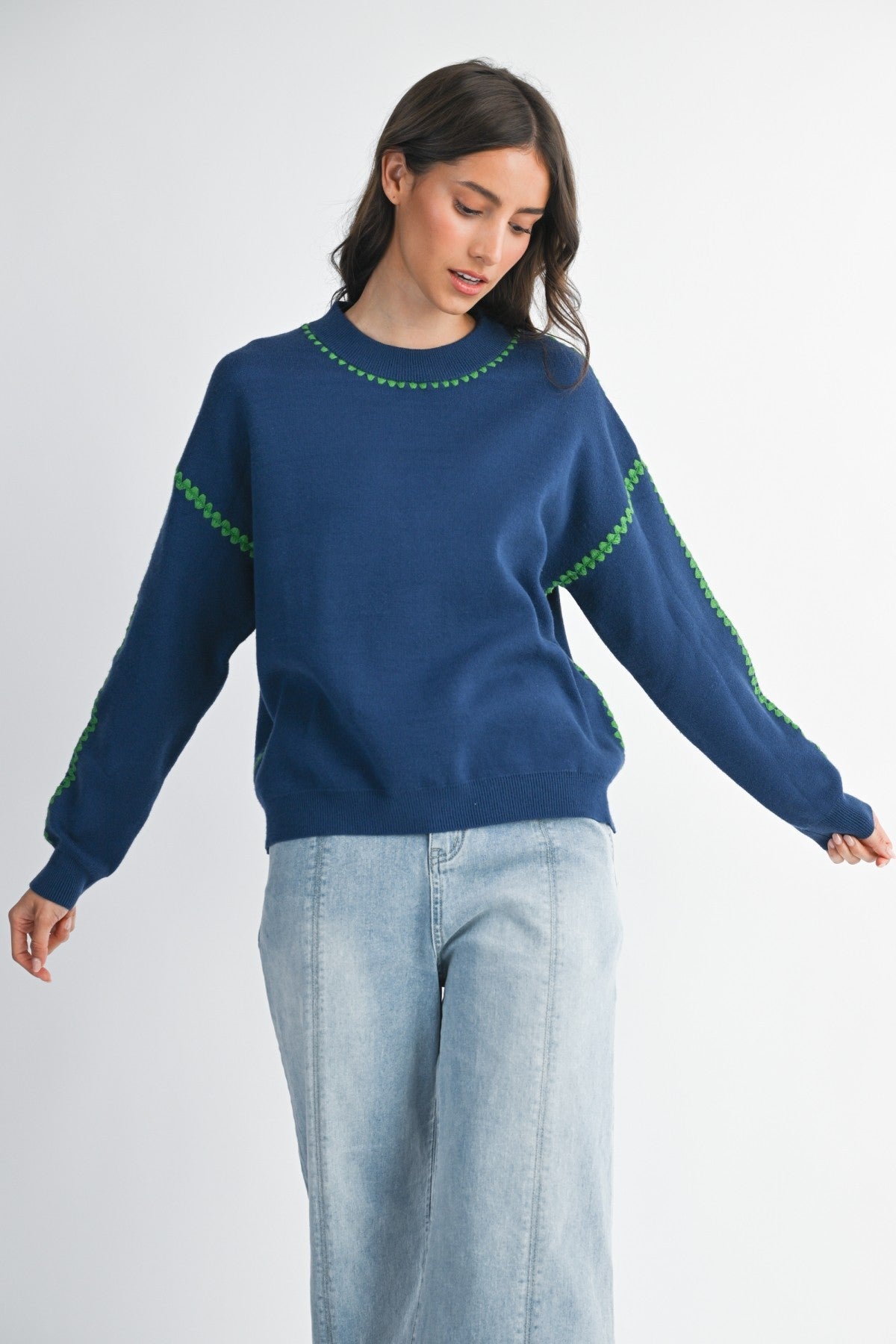 Woman wearing a royal blue sweater with green stitching on a white background