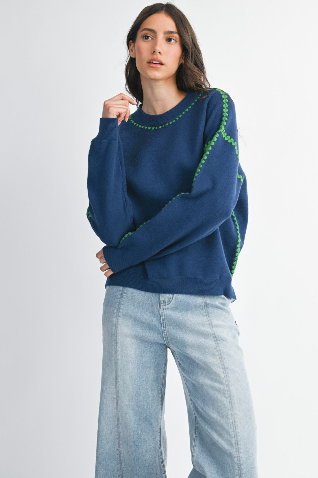 Woman wearing a royal blue sweater with green stitching on a white background