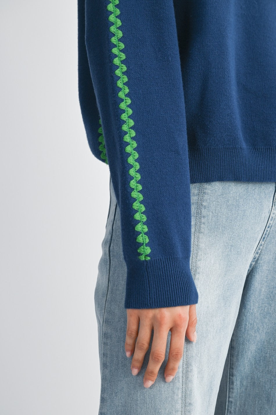 View of detail green stitching on royal blue sweater on a white background