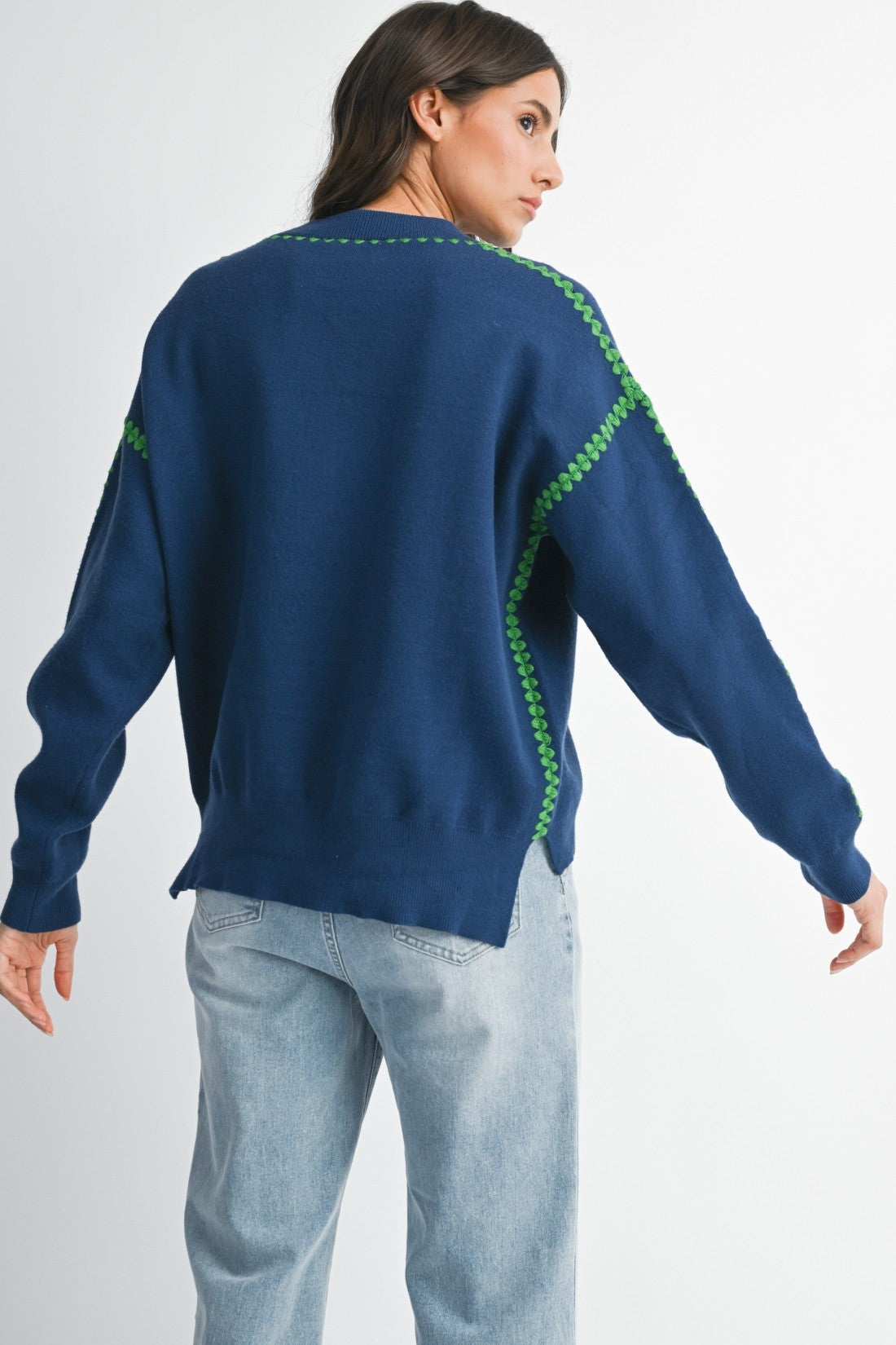 Back view of a woman wearing a royal blue sweater with green stitching on a white background