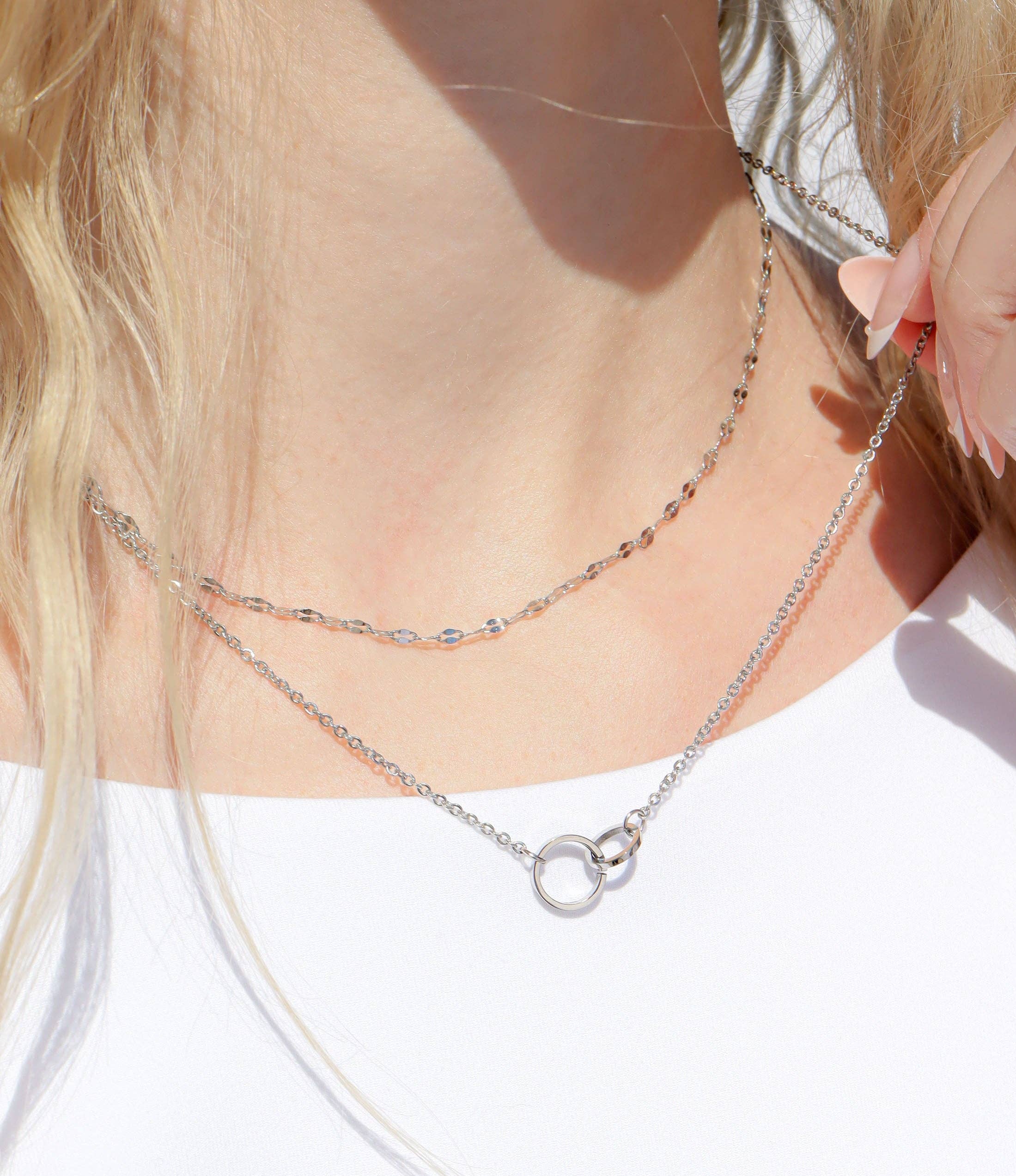 Close-up of a woman wearing a silver necklace with two interlocking rings