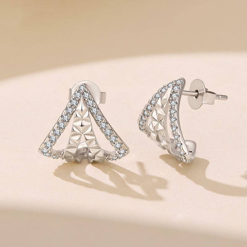 A pair of silver plated geometric triangle stud earrings adorned with cubic zirconia displayed on a warm beige surface with soft shadows.
