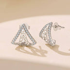 A pair of silver plated geometric triangle stud earrings adorned with cubic zirconia displayed on a warm beige surface with soft shadows.