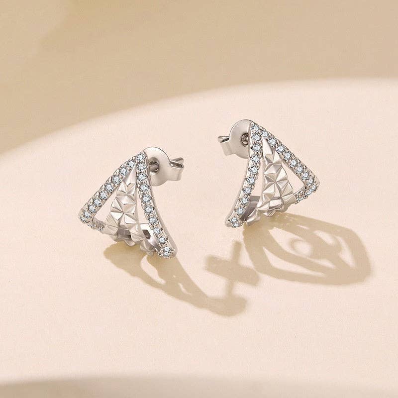 A pair of silver plated geometric triangle stud earrings adorned with cubic zirconia displayed on a warm beige surface with soft shadows.