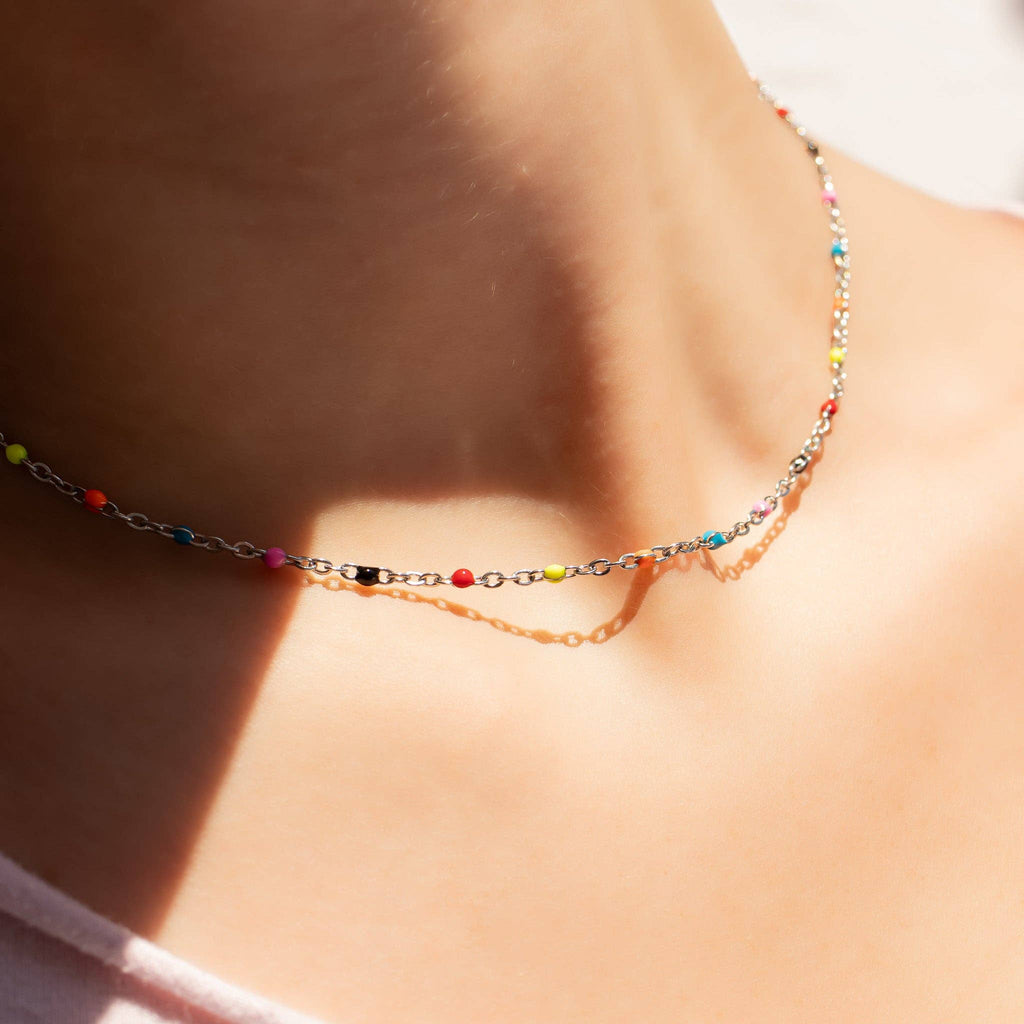 Woman wearing 18k gold stainless steel necklace with colorful beads 
against a neutral background