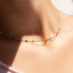 Woman wearing 18k gold stainless steel necklace with colorful beads 
against a neutral background