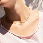 Woman wearing 18k gold stainless steel necklace with colorful beads in a light pink top.