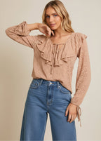 Woman wearing a taupe ruffle detail top with long sleeves and denim shorts on a beige background