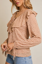 Woman wearing a taupe ruffled blouse and denim shorts on a beige background