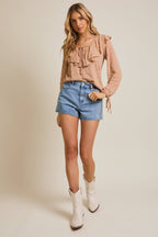 Woman wearing a taupe ruffled blouse and denim shorts on a beige background