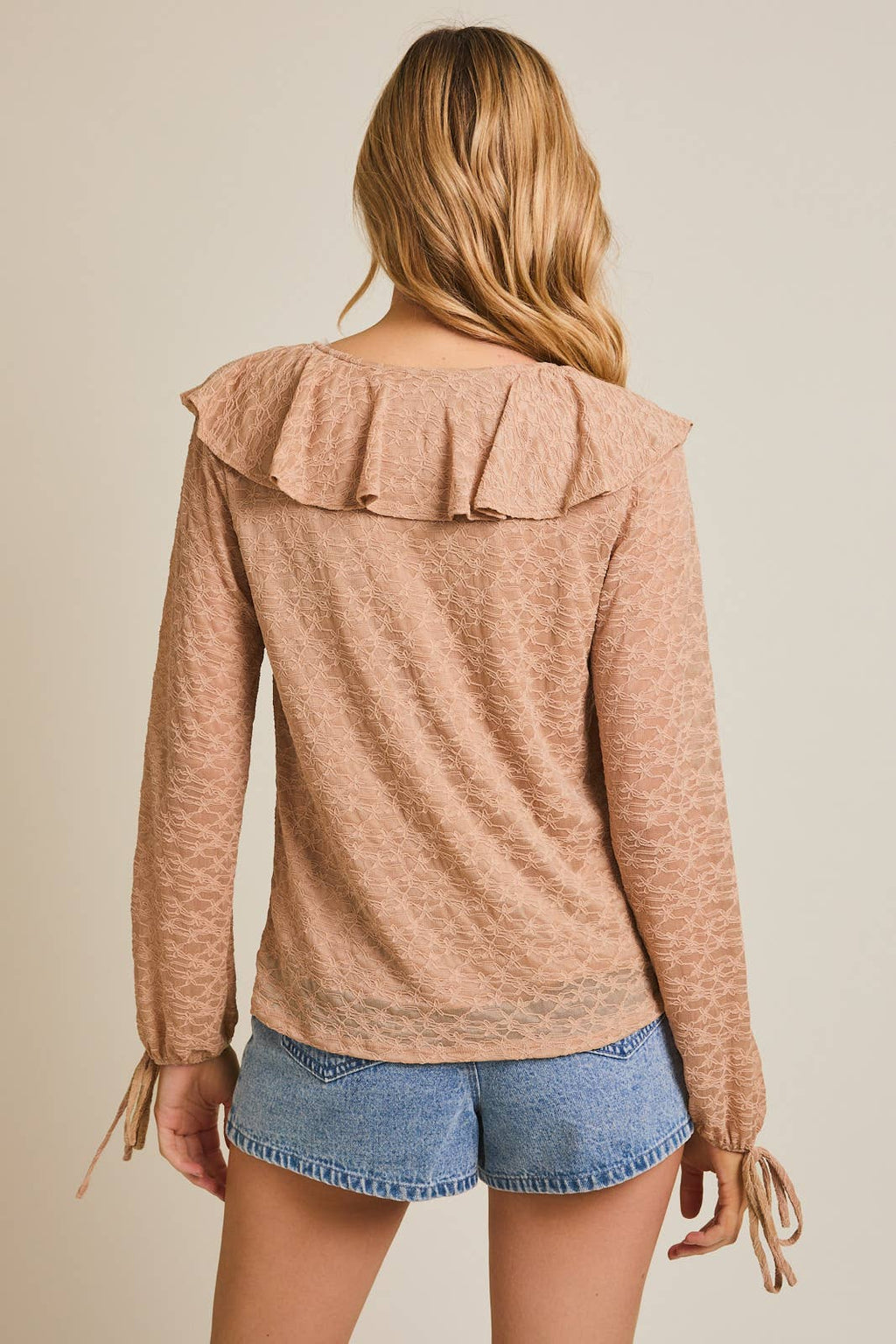 Woman wearing a taupe ruffled blouse and denim shorts on a beige background