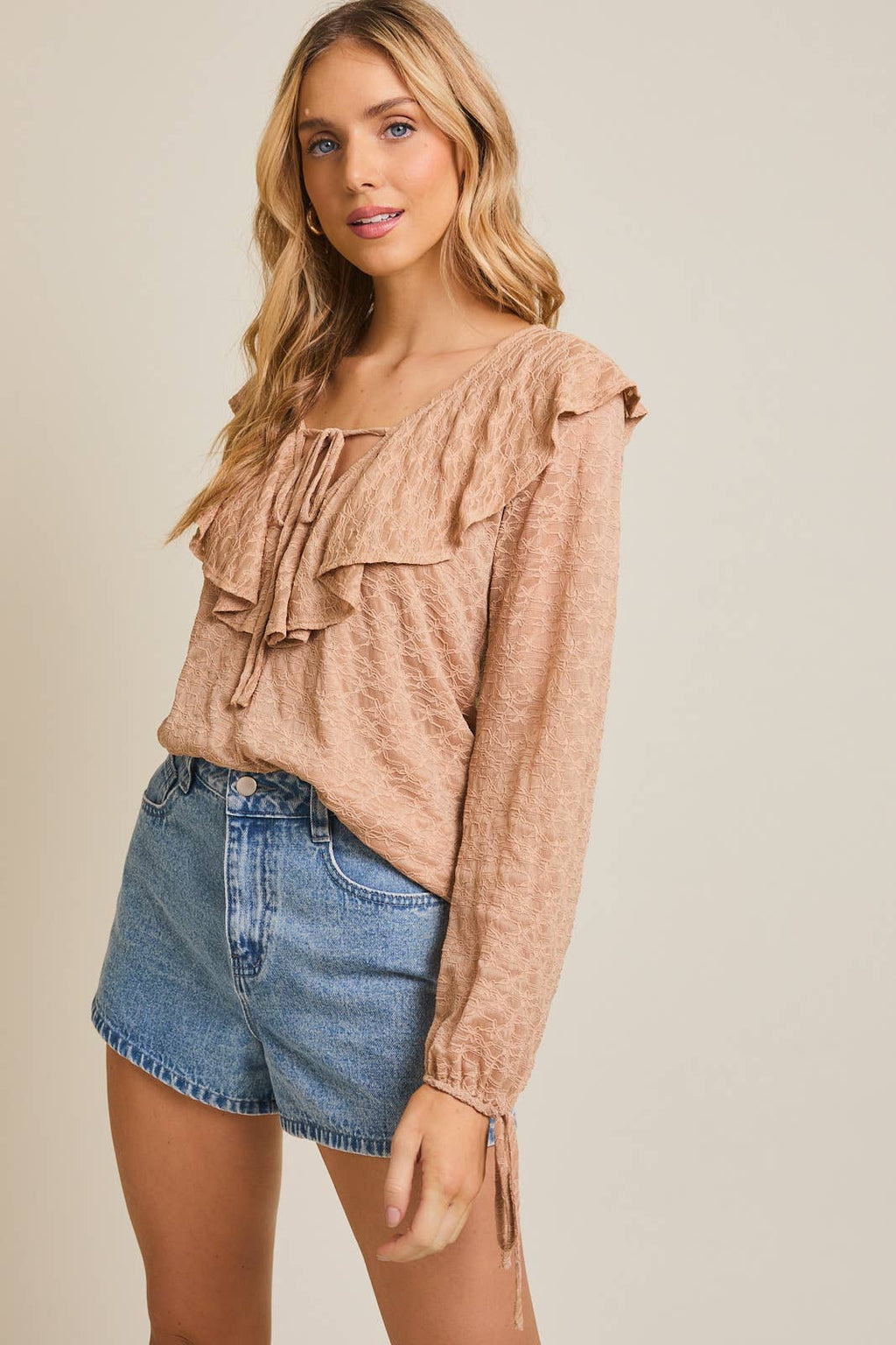 Woman wearing a taupe ruffled blouse and denim shorts on a beige background