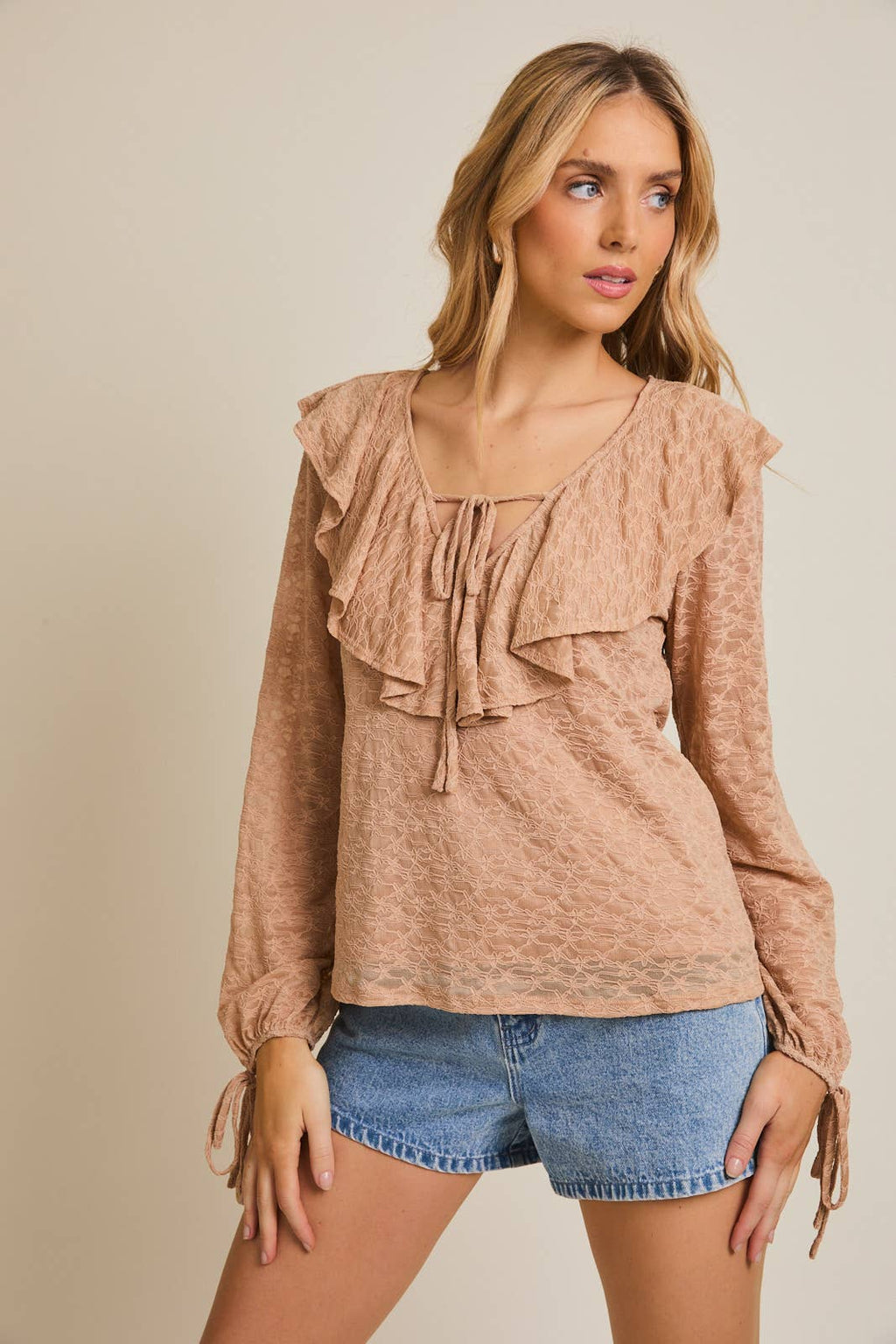 Woman wearing a taupe ruffled blouse and denim shorts on a beige background