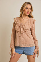 Woman wearing a taupe ruffled blouse and denim shorts on a beige background