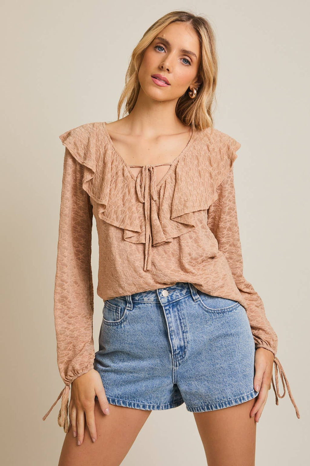 Woman wearing a taupe ruffled blouse and denim shorts on a beige background