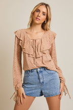 Woman wearing a taupe ruffled blouse and denim shorts on a beige background