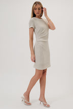 Woman wearing a beige boucle knit dress with side pleats on a white background